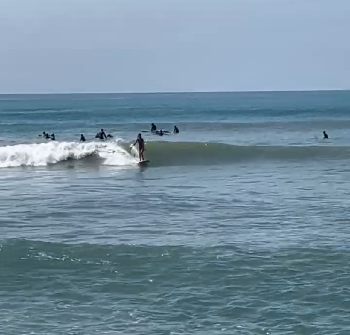 A surfer rides the waves at the beach, surrounded by several other individuals in the water.